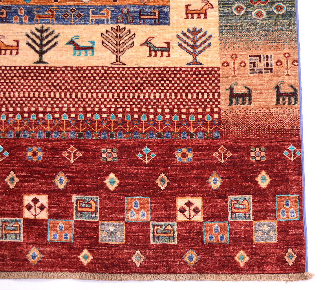 A close-up of a corner of a handmade multicolour Loribaft rug showing multiple horizontal bands with geometric and animal motifs in red, beige, blue, orange, and brown, with a fringed edge visible at the bottom.