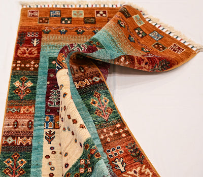 Loribaft Gabbeh rug draped with turquoise and rust bands, multicolour patterns, and fringed edge along the top of the picture.