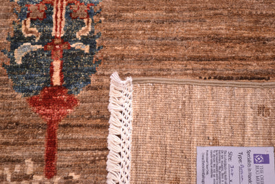 Close-up of a corner turned up showing handknotting weave of a Pictorial Afghan Loribaft carpet showing a tan and brown textured base, a partial blue and red decorative motif, white fringe, and a product label.