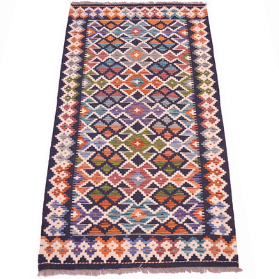 A rectangular colourful Kilim handwoven rug with a vibrant geometric diamond pattern in orange, blue, green, purple, and cream, featuring a dark navy border and fringed edges.
