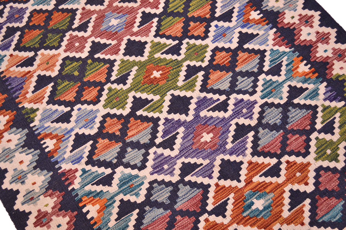 A close-up of a handwoven colourful kilim rug featuring a geometric diamond pattern in midnight blue, orange, green, purple, and cream.