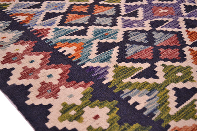 A close-up of a Afghan woven colourful kilim rug showing its detailed geometric and floral patterns in navy, beige, green, orange, and purple.