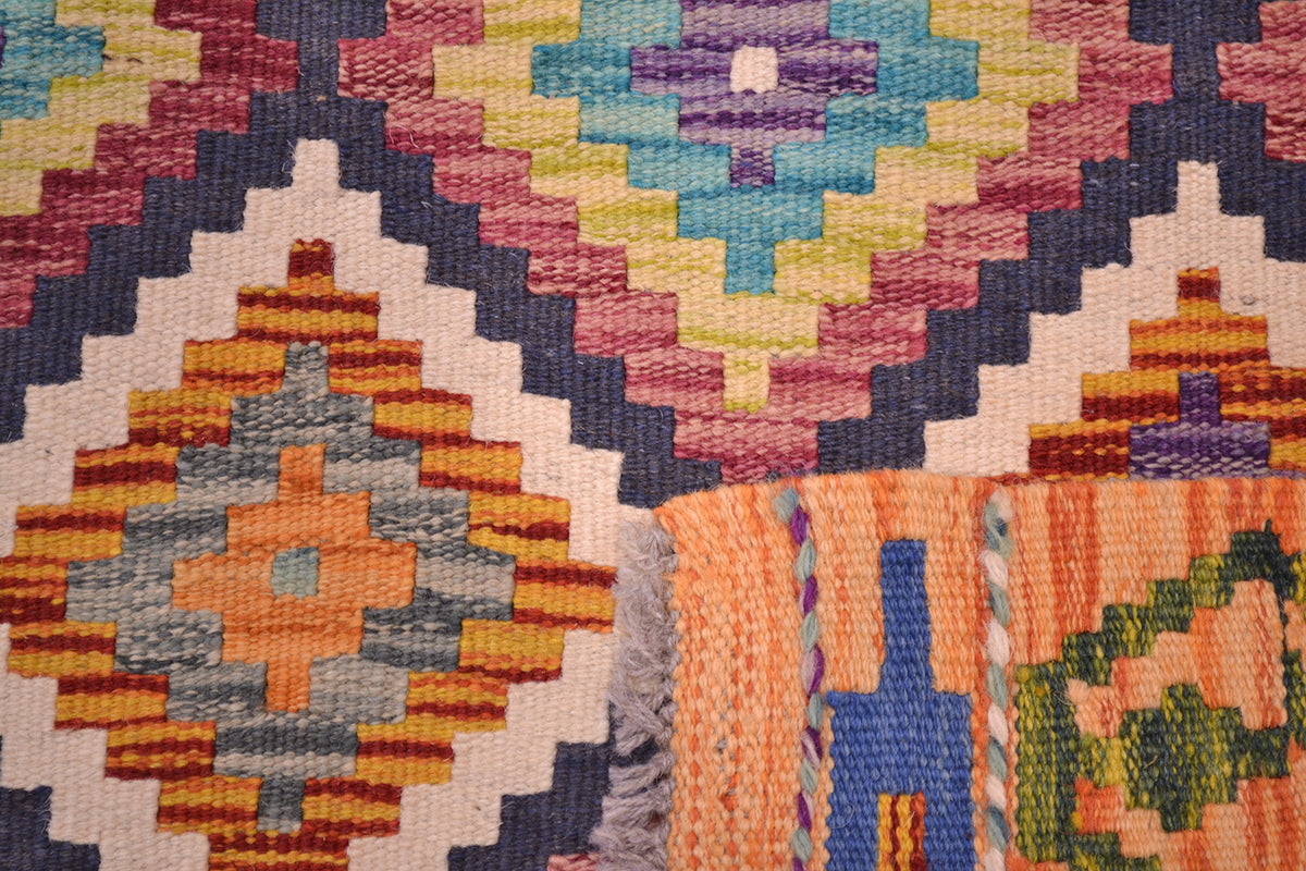 Close-up of the weave of a handwoven Afghan Maimana Kilim short runner with a colourful geometric pattern, showing orange, blue, pink, yellow, green, and cream threads in a detailed rug.