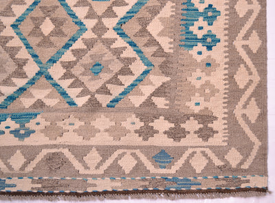A close-up of a handwoven large Afghan Kilim rug showing a geometric pattern in beige, grey, and turquoise blue, with a fringed edge visible at the bottom.