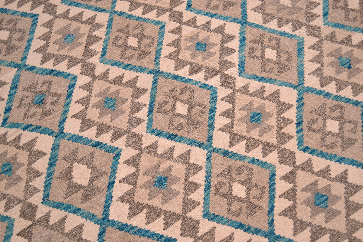 A close-up of a handwoven Kilim rug with a repeating geometric tribal style pattern in beige, brown, and turquoise blue.