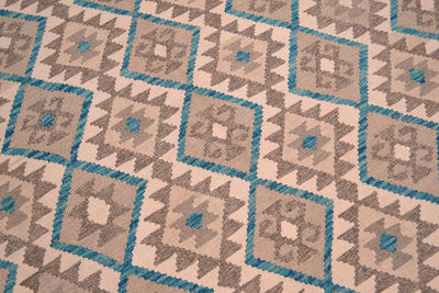 A close-up of a handwoven Kilim rug with a repeating geometric tribal style pattern in beige, brown, and turquoise blue.