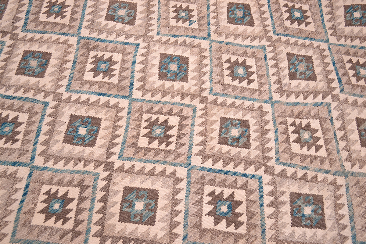 A close-up of a woven large Kilim rug featuring a repeating geometric pattern in beige, brown, teal, and cream.