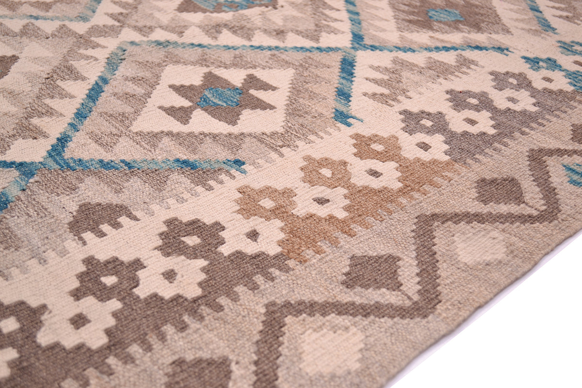 A close-up of a woven 12x9 Kilim rug with a geometric in beige, brown, and teal shown on a white surface.