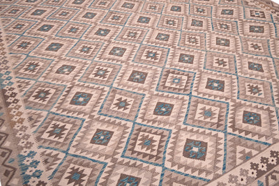 A close-up view of a handwoven large Afghan Kilim rug with a repeating geometric pattern in beige, brown, grey, and teal.