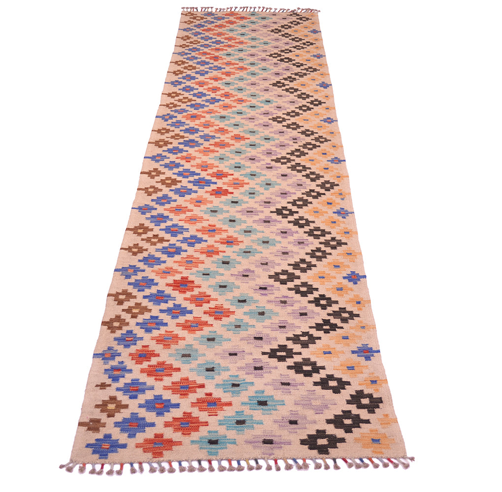 A 13 foot long Afghan kilim runner rug with a geometric diamond pattern in orange, blue, brown, black, and light blue on a beige background, finished with tassel fringe on both ends.