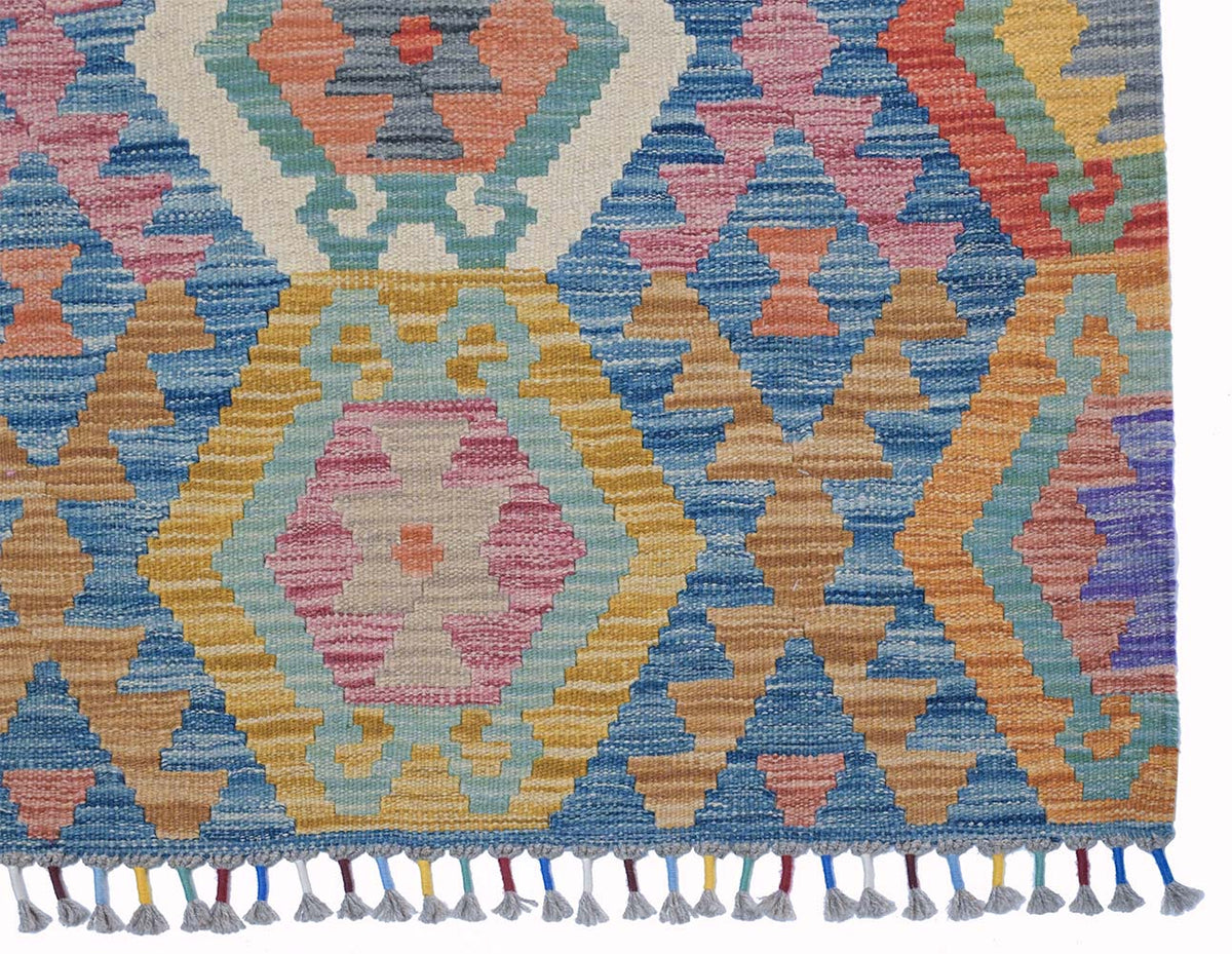 A close-up of a corner  Giant Handwoven Afghan Kilim rug with a colourful geometric pattern and tassel fringe along the bottom edge.