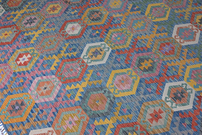 A close-up of a Giant Handwoven Afghan Kilim rug with a colourful geometric pattern featuring hexagons and stars in blue, pink, yellow, orange, and white.