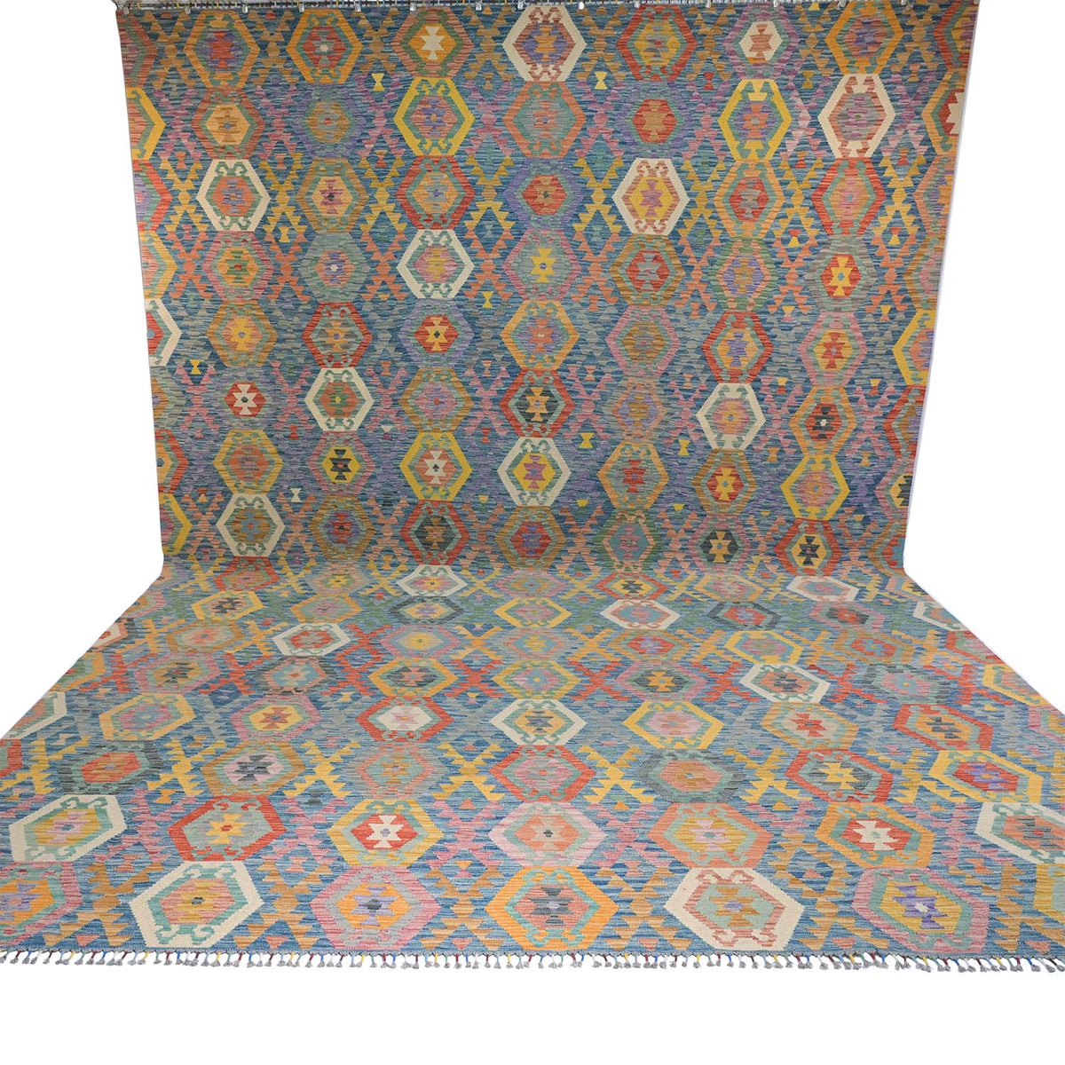 A Giant Handwoven Afghan Kilim rug with a colourful geometric diamond pattern, shown draped to display both its flat surface and its fringed edge against a white background.