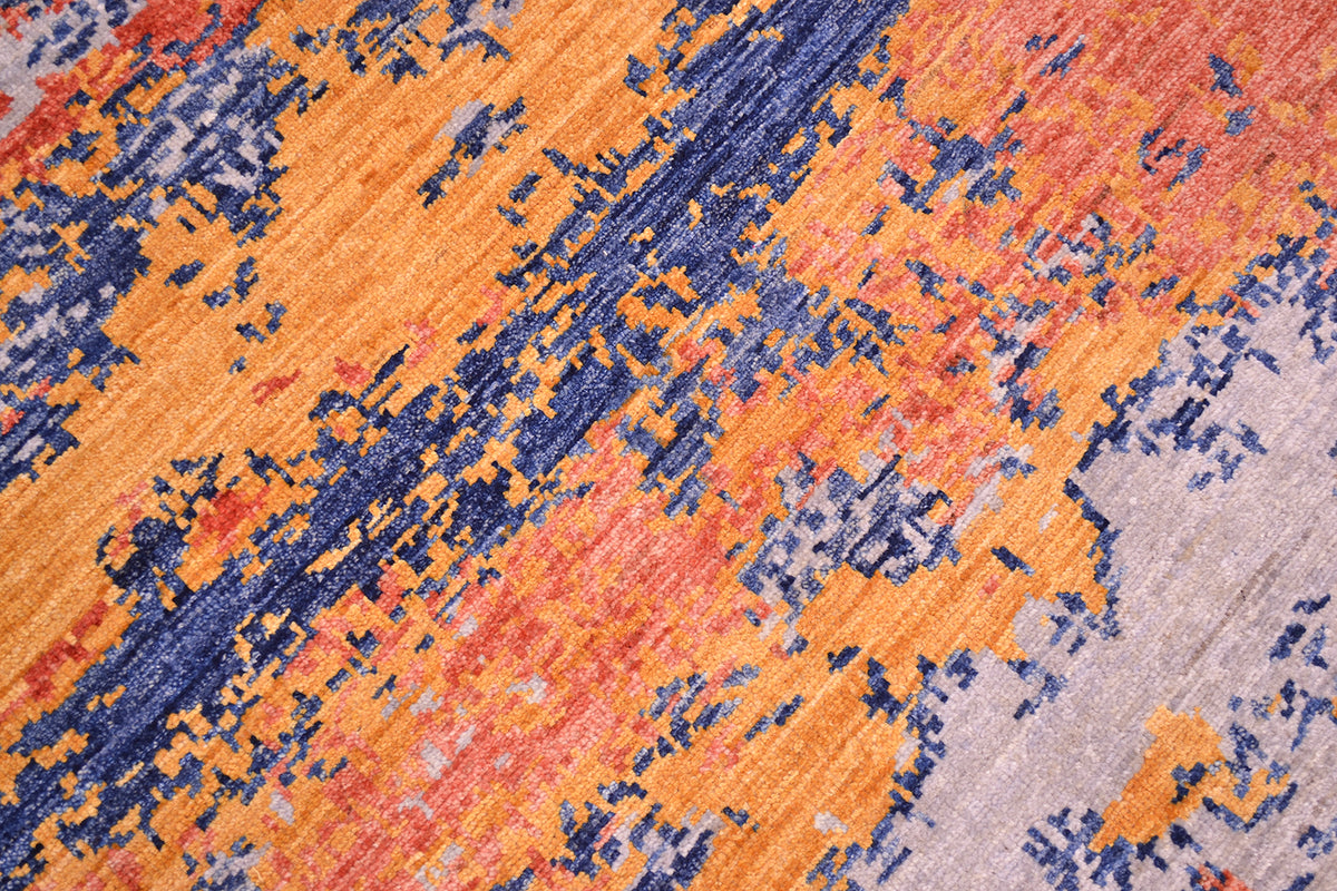 Close up detail of abstract rug with fragmented design with terracotta, golden amber, stone grey wth deep sea blue. Handknotted pile and artisan dyes.