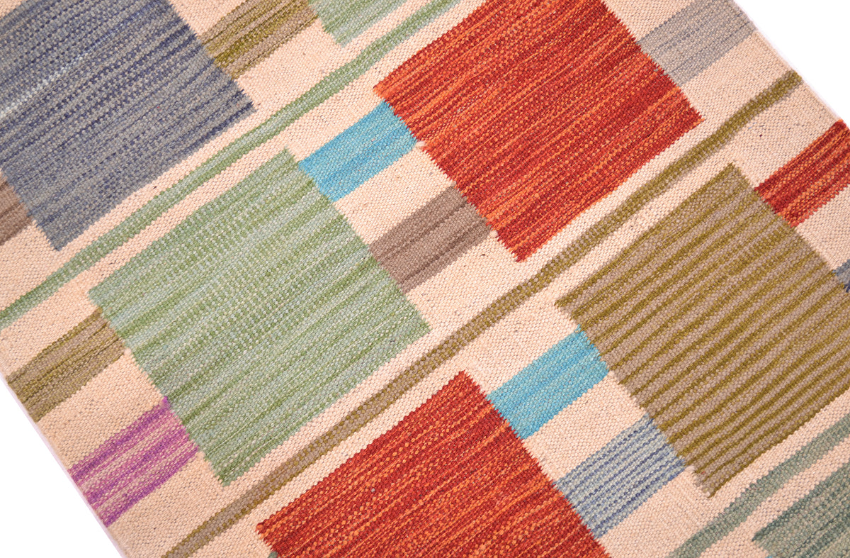 A close-up of a woven Modern Kilim short runner with a geometric contemporary pattern in muted tones of red, green, blue, beige, brown, and purple on a light cream background.