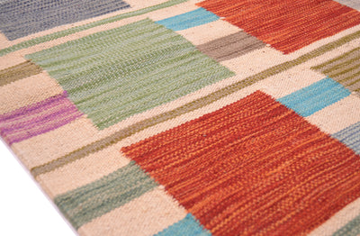A close-up of a handwoven modern Afghan Kilim runner with a geometric design in orange, green, blue, purple, beige, and grey.