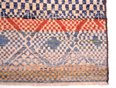 Corner detail of Handknotted carpet wirh cream and blue  geometric patterning. Fringe showing pure wool warps.