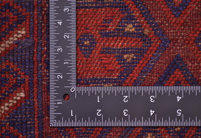 A close-up of the weave of a patterned handmade Afghan Mushwani rug with a dark metal L-shaped ruler displaying the scale of the weave, and showing a red and navy blue woven design.