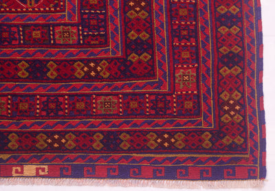 A close-up of a fine Afghan rug corner showing deep red, navy blue, and tan geometric motifs with white fringe along the bottom edge.
