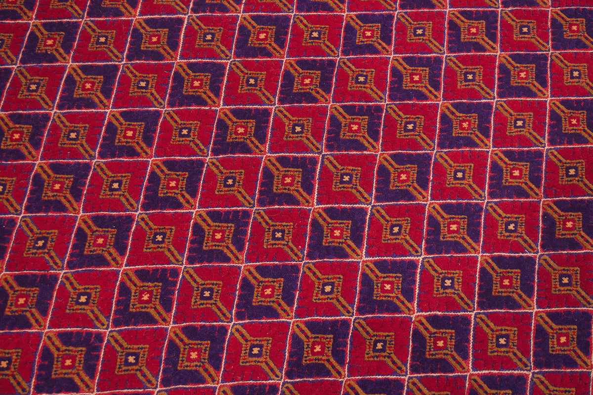 A close-up of a fine Mushwani rug / carpet with a repeating geometric diamond pattern in red, purple, orange, and cream.