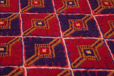 A close-up of a fine Afghan Mushwani rug featuring red and dark purple squares outlined with gold geometric accents and separated by white lines.