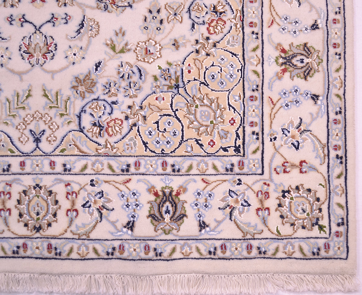 Close-up of an ornate Nain rug corner showing a cream base with intricate floral and scroll motifs in blue, green, red, and beige, finished with a fringed edge.