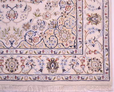 Close-up of an ornate Nain rug corner showing a cream base with intricate floral and scroll motifs in blue, green, red, and beige, finished with a fringed edge.