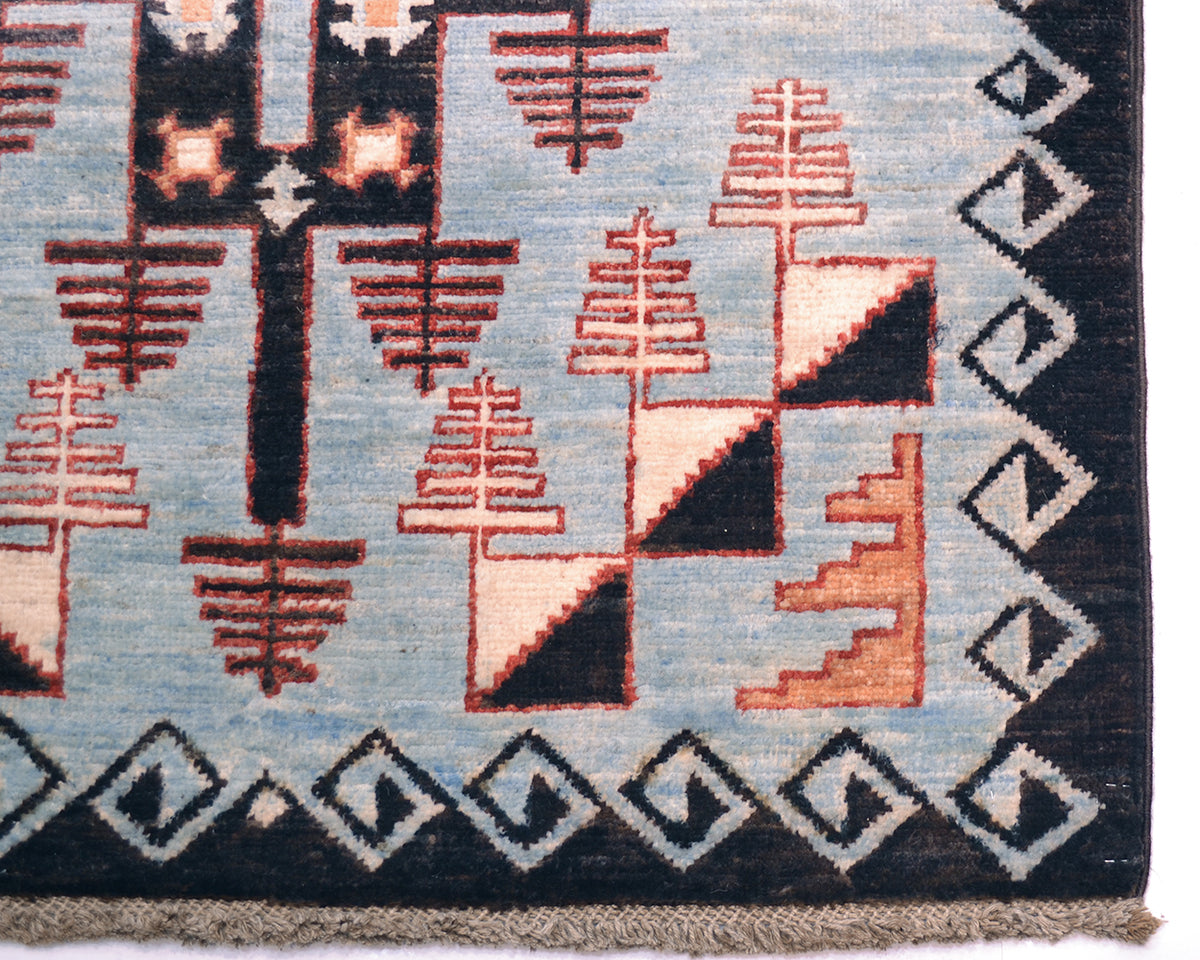 Close-up of a corner of an Afghan Blue Aryana long runner showing a geometric pattern with stylised tree-like shapes in terracotta, cream, and black on a light blue field, with a dark border and fringe.
