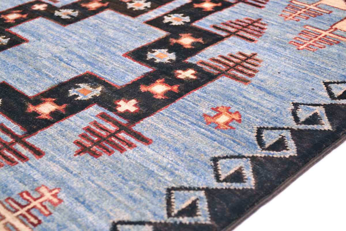 A close-up of a hand-knotted Afghan Blue Aryana long runner with a light blue field, black geometric steps, and red and white diamond and cross motifs.
