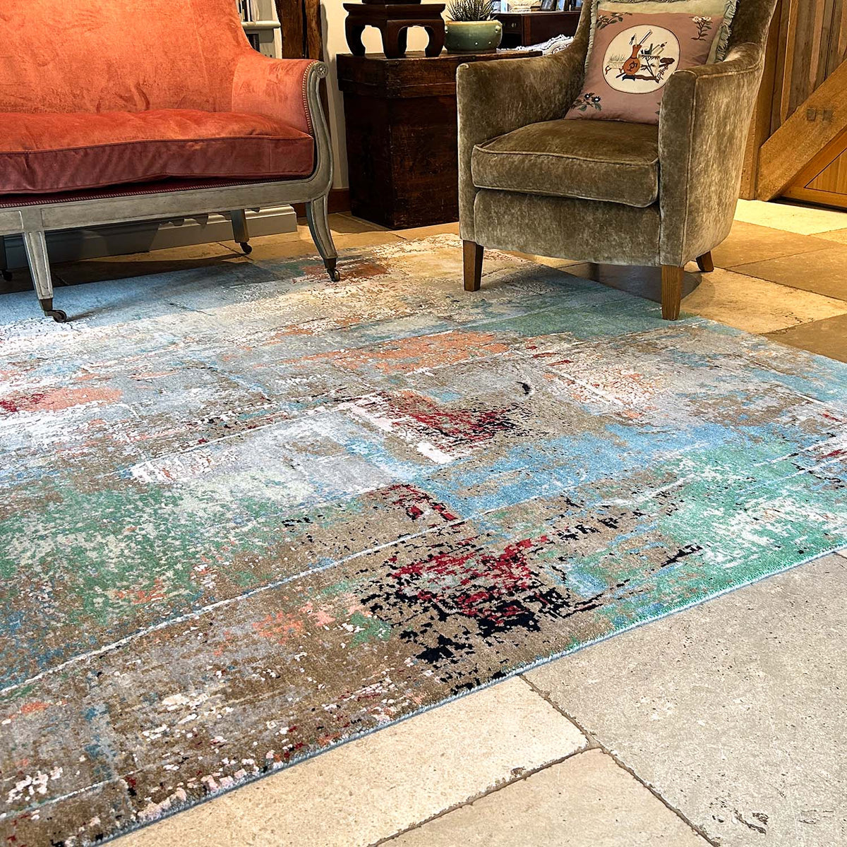 Abstract hand-knotted wool and silk handwoven Textural Oasis carpet with multi-colour modern design in green, red, black, orange, brown, blue and cream set in living room on a stone floor.