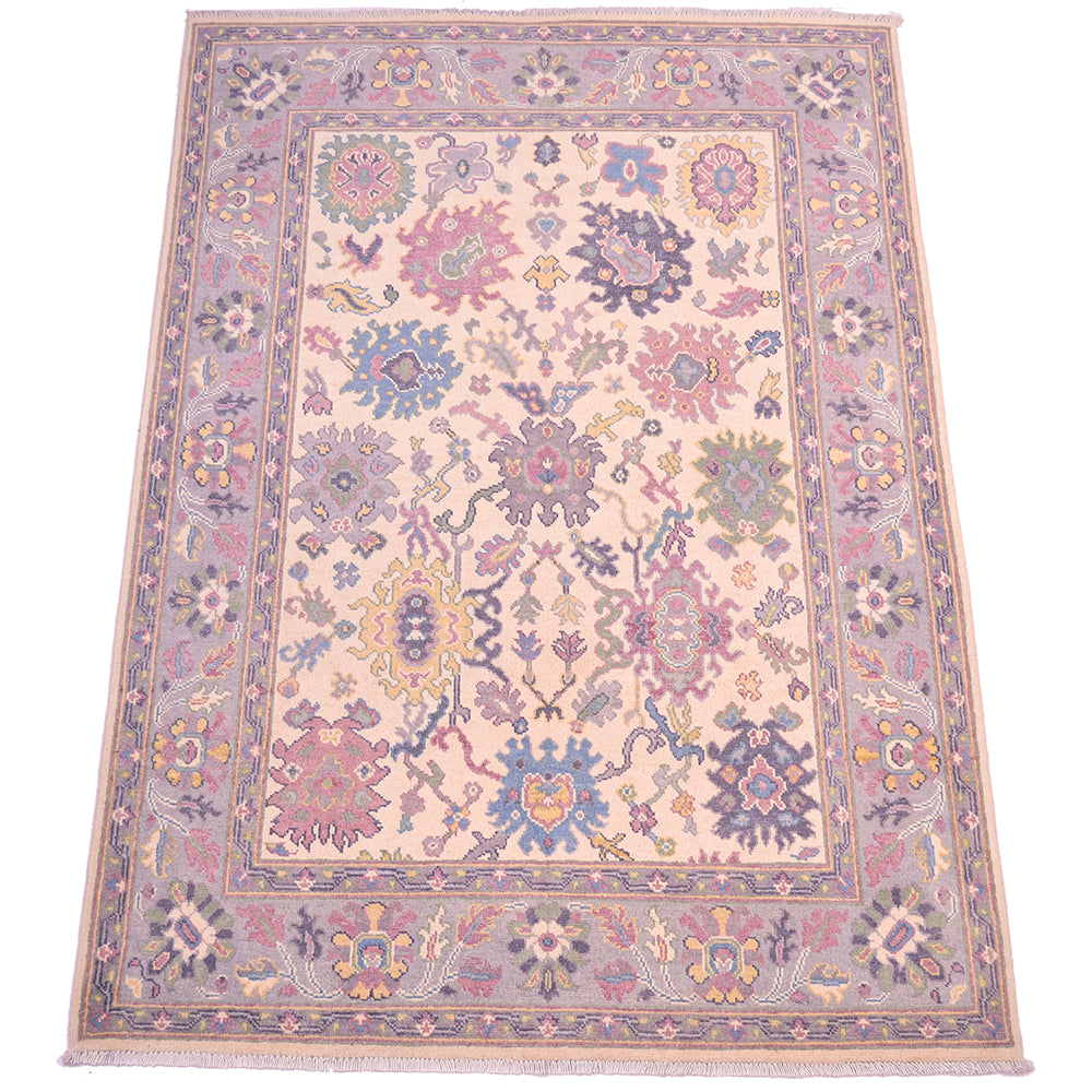 Handmade Oushak rug with ornate floral border, cream field in mauve, blue, and pink.