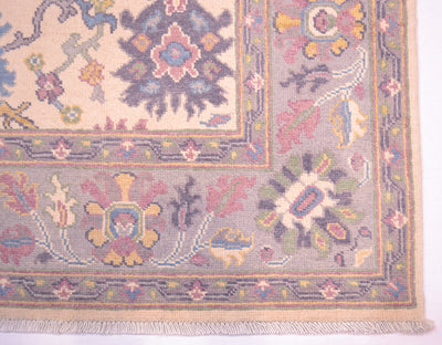 Handmade Oushak rug corner detail with floral motifs and multicolor frame on cream ground.