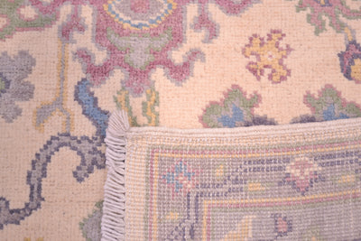 Handmade Oushak rug with fringed edge; multicolor floral pattern on cream field.