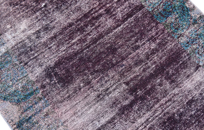 Close up detail of vintage distressed overdyed carpet with exposed cotton warp and wefts with areas of intentioanl zero pile with teal green boteh motifs in border. Main deep purple aubergine field colour.