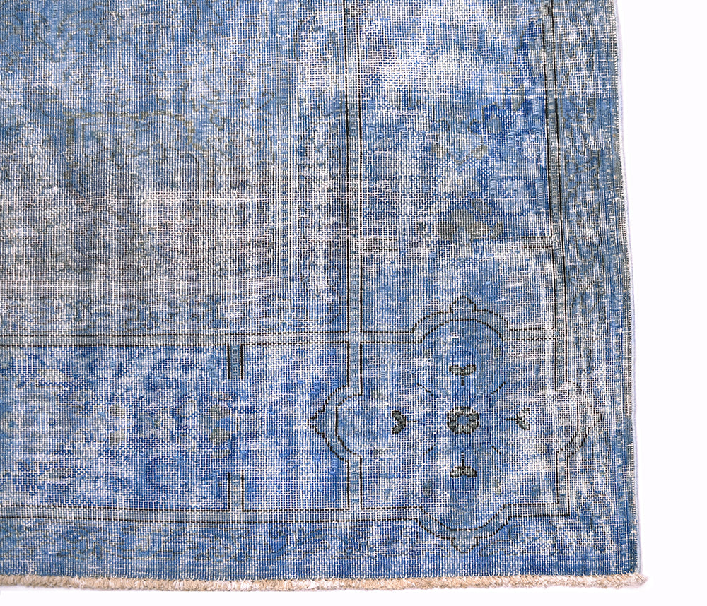 Corner detail of vintage blue overdyed carpet  with charocal outling the border lines of ghost like floral detailing in border and field. Vintage distressed-look pile.
