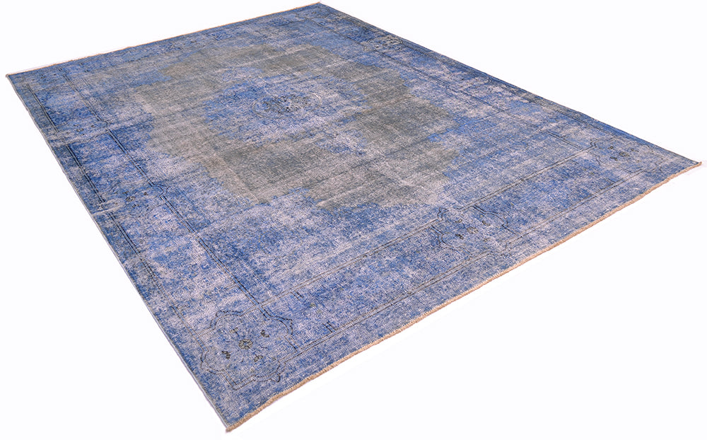 Angled view of vintage overdyed carpet with traditional design. Re-dyed with blues and greys. Outling of border in dark charcoal. Angled viewpoint with a white background.