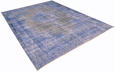 Angled view of vintage overdyed carpet with traditional design. Re-dyed with blues and greys. Outling of border in dark charcoal. Angled viewpoint with a white background.