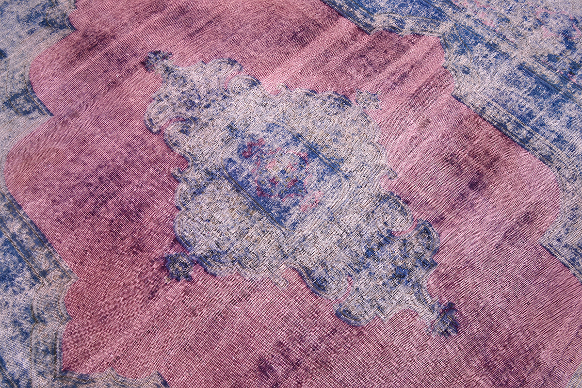 Close up detail of central medallion morif of overdyed carpet in blue and fushia tones. Clours of magenta and raspberry pink and echoing scalloped cemtral medallion motif. Handwoven zero pile.