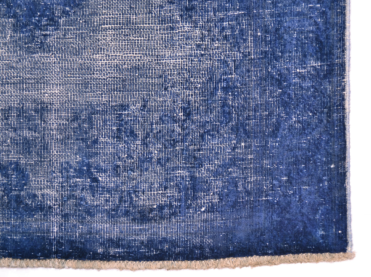 A close-up of a distressed blue runners corner showing its woven texture, faded pattern, and a fringed edge on a white background.