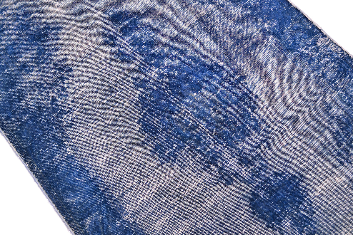 A close-up of a distressed blue and white patterned runner, showing its woven texture and faded traditional motifs.