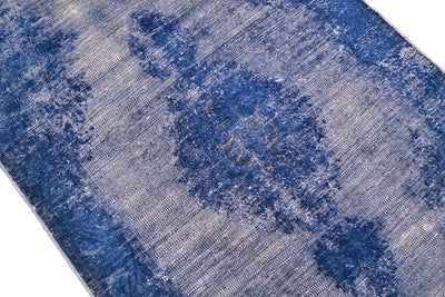A close-up of a distressed blue and white patterned runner, showing its woven texture and faded traditional motifs.