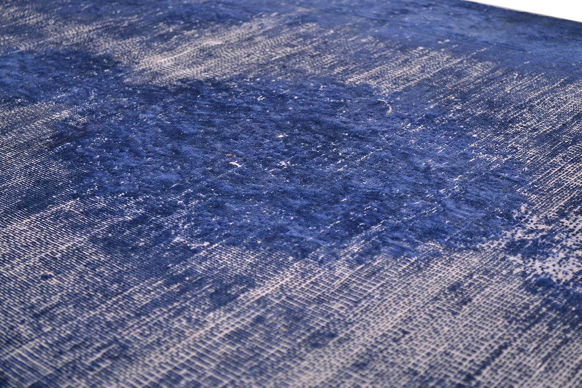 A close-up of a textured area runner featuring a distressed, floral  pattern in shades of navy blue and off-white.