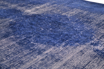 A close-up of a textured area runner featuring a distressed, floral  pattern in shades of navy blue and off-white.