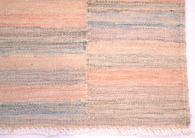 Corner detail of pastel abrash kilim rug with details of narrow stripes and woven flatweave with cotton fringe warp threads.