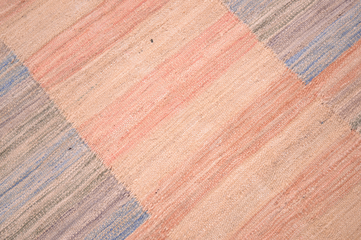 Close detail of handwoven flatweave pastel coloured rug wih blue greys, coral pinks and apricots  with subtlely striped geometric patterning. 
