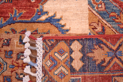 Close-up of the underside corner of a hand-knotted Afghan Patchwork design patterned rug showing cream, rust red, blue, and tan woven motifs with white tassels along the edge.