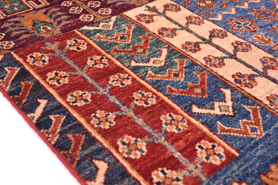 A close-up of a patterned patchwork design area rug with vertical bands of rust red, navy blue, beige, and orange geometric and floral motifs.