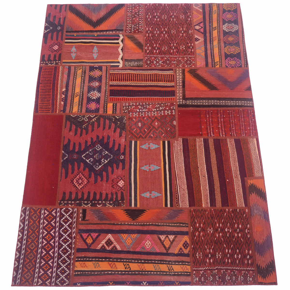 A rectangular patchwork kilim rug featuring a collage of traditional geometric and tribal patterns in deep reds, rust orange, burgundy, and black, laid flat against a white background.