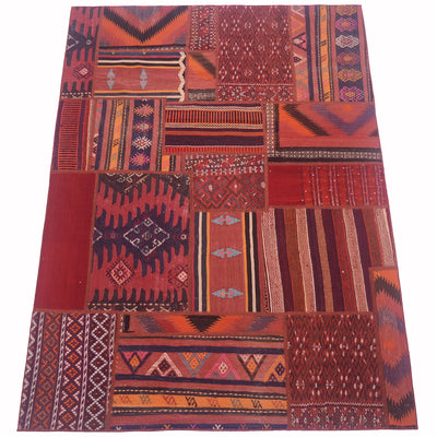 A rectangular patchwork kilim rug featuring a collage of traditional geometric and tribal patterns in deep reds, rust orange, burgundy, and black, laid flat against a white background.