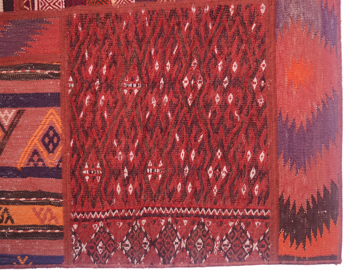 A close-up of a handwoven Patchwork Kilim rug showing a red central field with repeating diamond and zigzag motifs, bordered by multicoloured geometric patterns in orange, purple, brown, and cream.